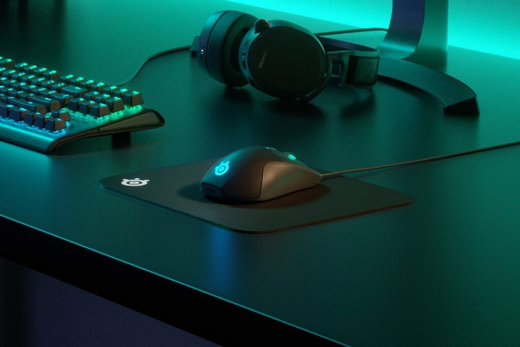 Tapis de souris SteelSeries QcK Mini avec souris et clavier rétroéclairé sur un bureau gaming.